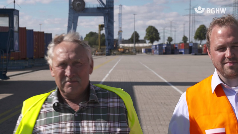 Zwei Lübeker-Hafen-Gesellschafts Mitarbeiter in Warnwesten laufen auf die Kamera zu