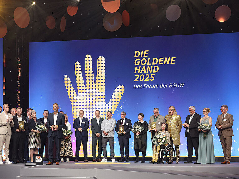 Preisverleihung DIE GOLDENE HAND 2025 in Mannheim. Die Preisträger stehen gemeinsam auf der Bühne. Die Moderatoren im Vordergrund.