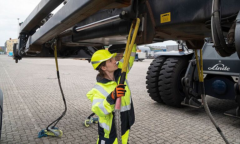 Hafenarbeiterin beim Anlegen von schweren Ketten an eine Projektladung