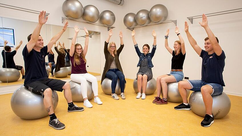 Eine Gruppe von Auszubildenen der Firma Trixie Heimtierbedarf sitzen auf Pezibällenin einem Sportraum und machen gymnastische Übungen.