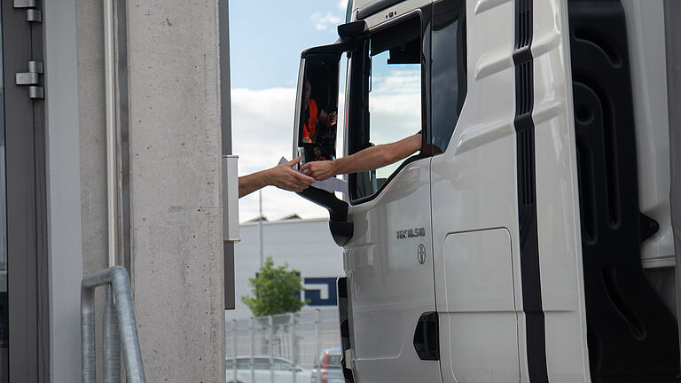 LKW-Fahrer überreicht L’ORÉAL-Mitarbeiter bei der Ausfahrt ein Dokument. 
